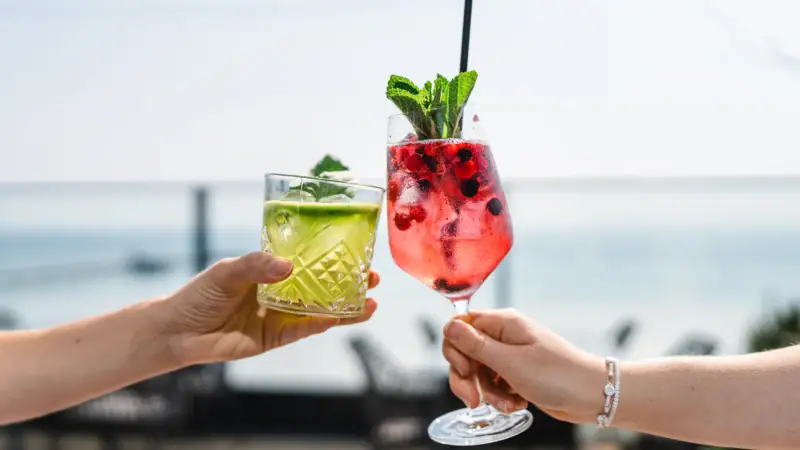 Hands holding cocktails with fruit garnishes.