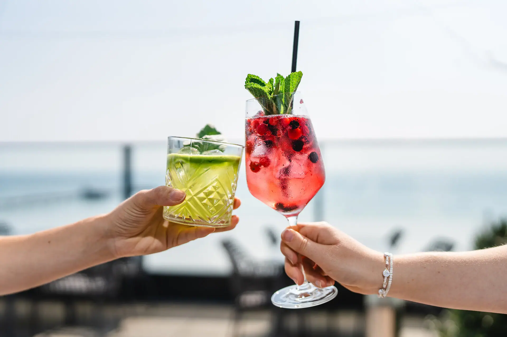 A pair of hands holding cocktails with fruit garnish.