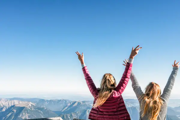 View Zugspitze Two women with their arms raised, looking up to the sky.