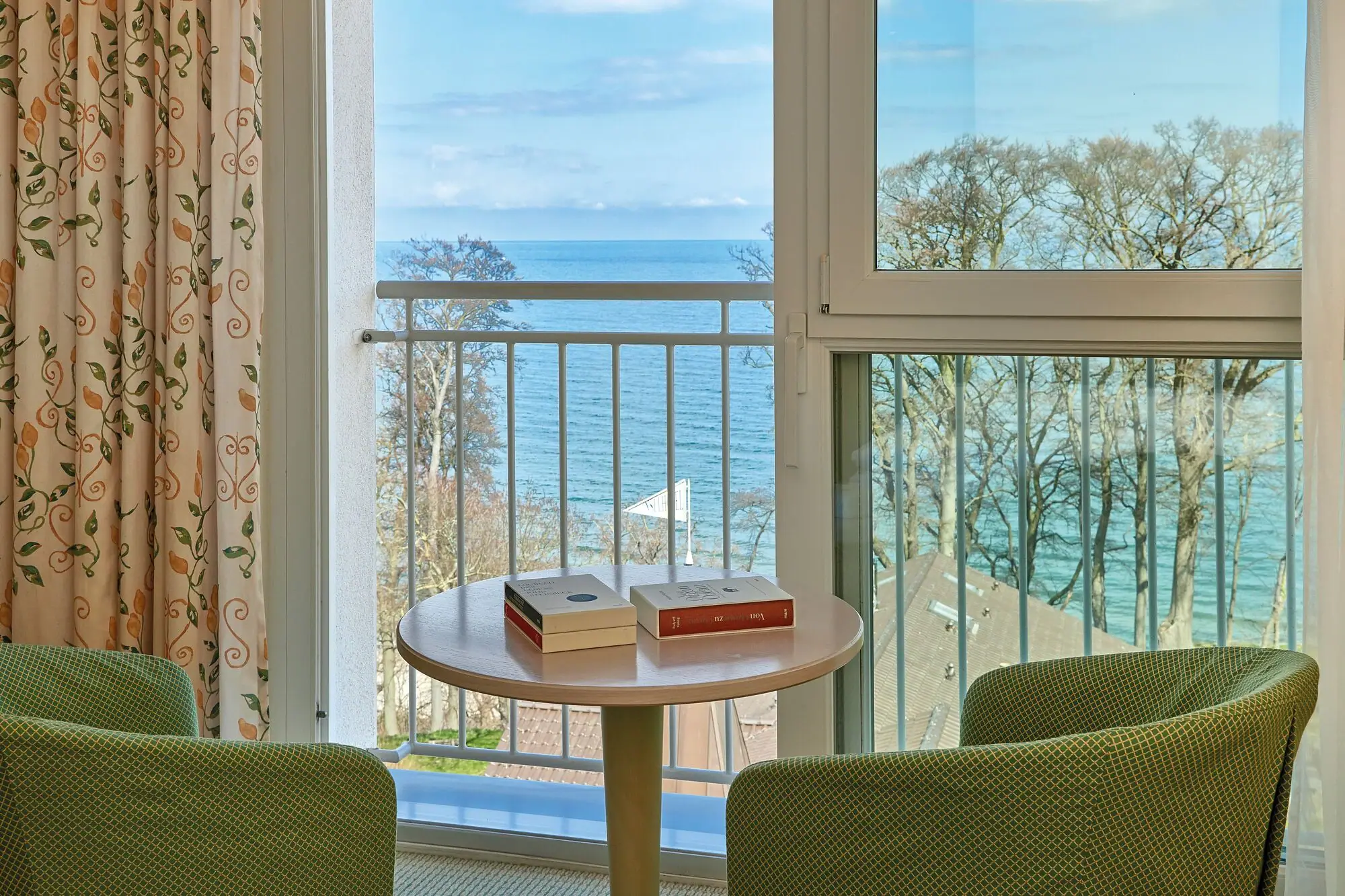 A table with books on it, in the background a window with a view of the ocean.