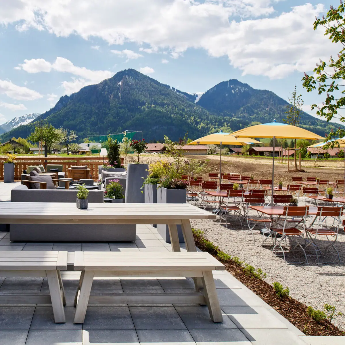 A terrace with tables and chairs in front of a mountain in the background.