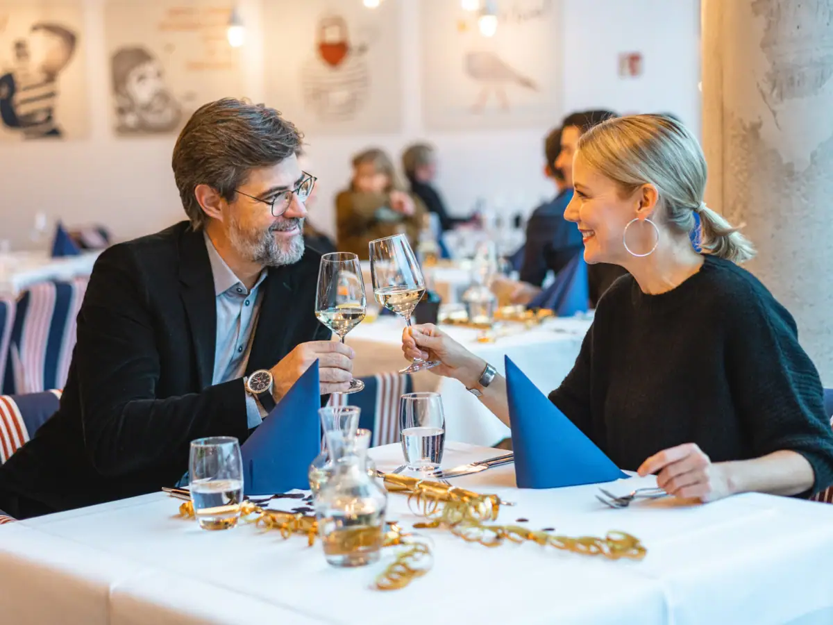 A man and a woman are sitting at a table with glasses of wine.