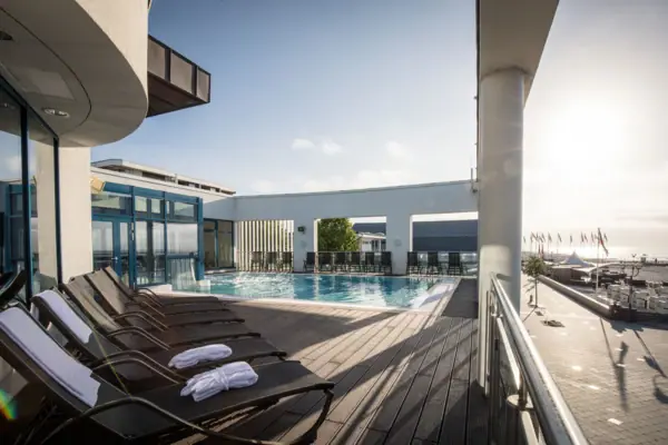 A pool with sun loungers and a deck in the spa area of the aja Grömitz or the Grömitzer Welle...