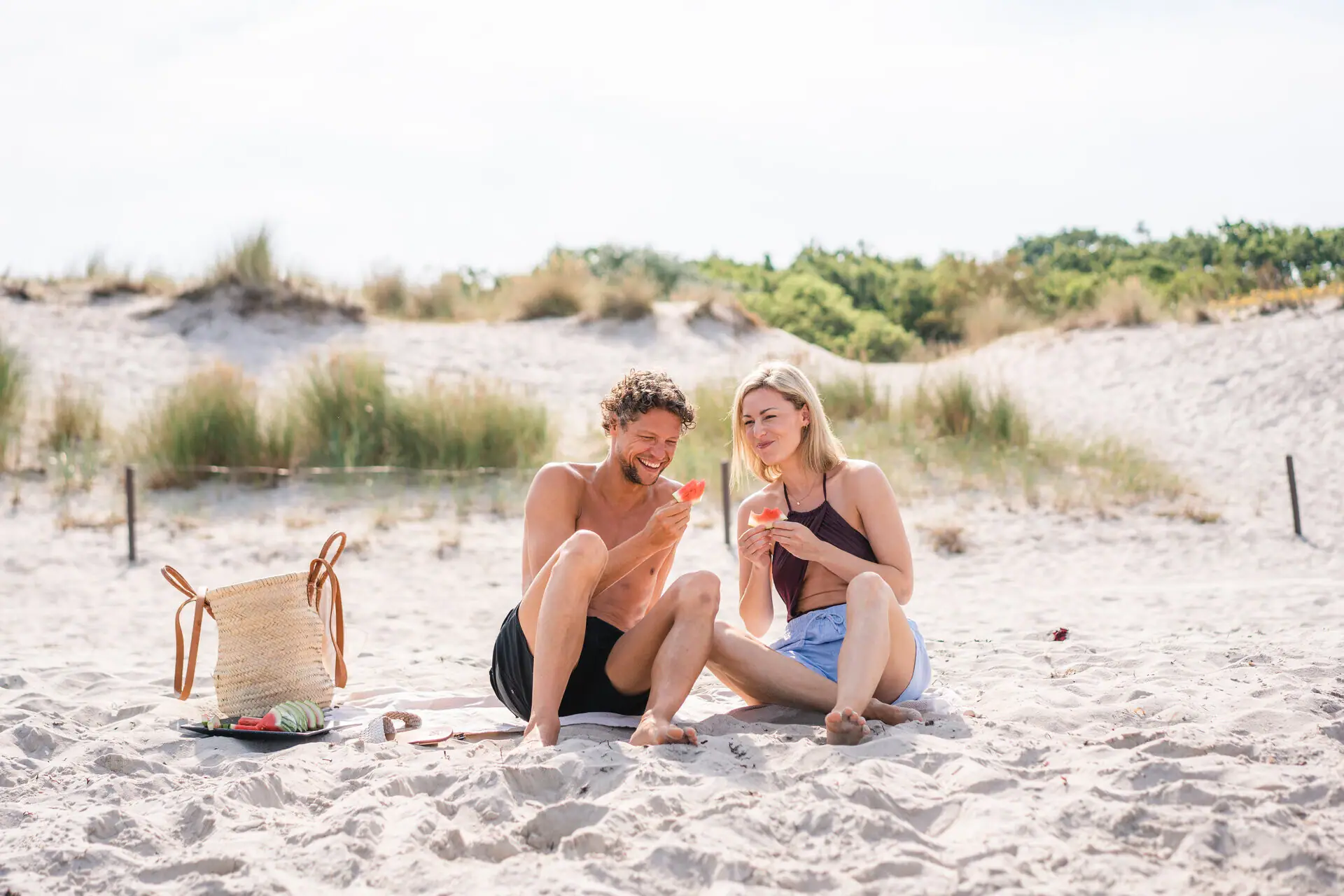A couple sits happily on a sunny Baltic Sea beach enjoying watermelon. 