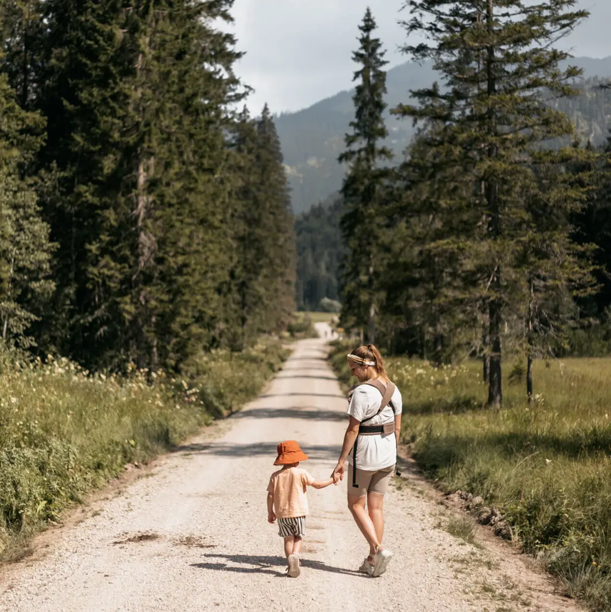 A woman and a child are walking along a dirt track lined with trees.