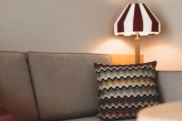 A lamp with a striped lampshade stands next to a sofa.