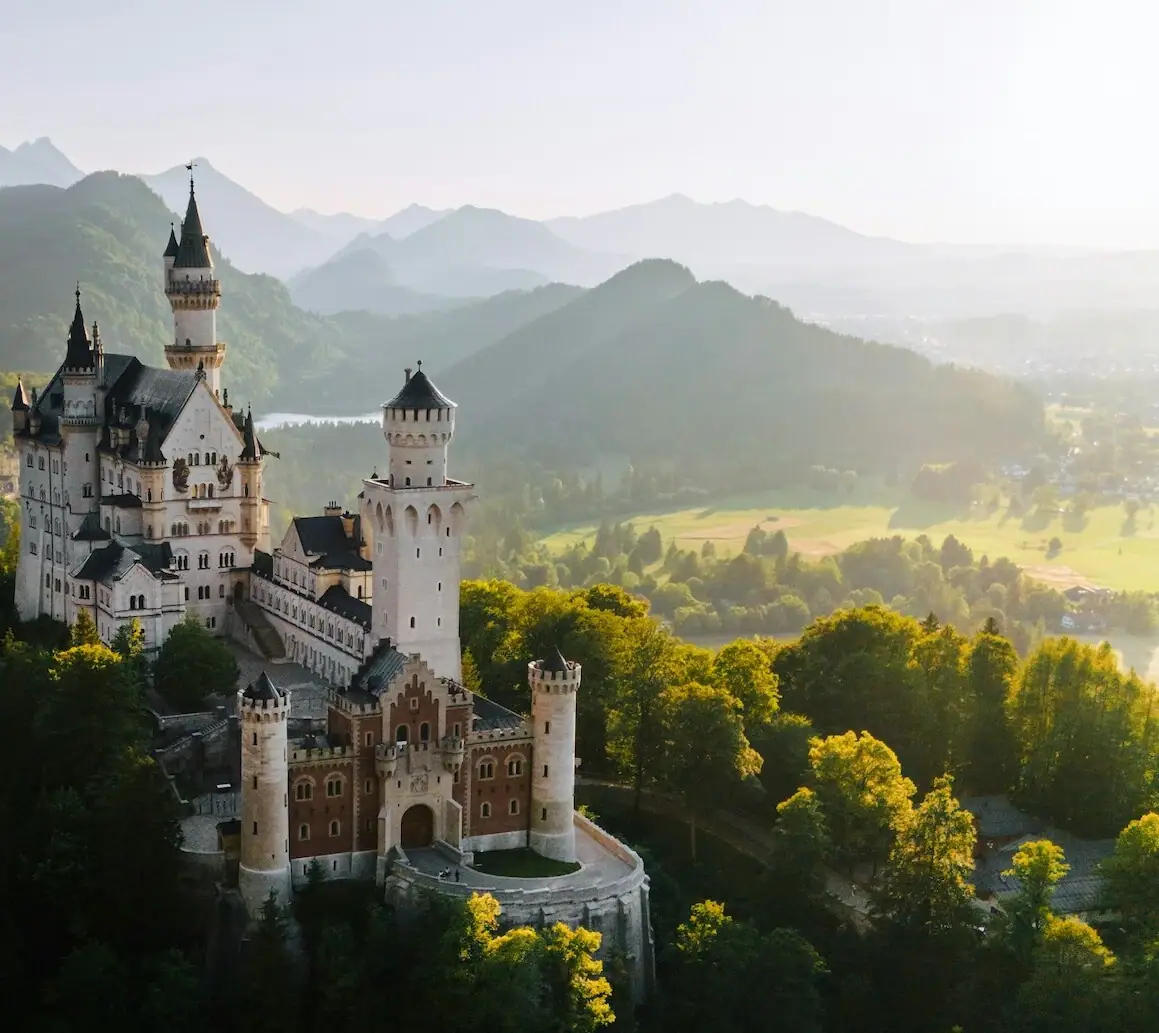 Neuschwanstein Castle Neuschwanstein Castle on a hill with trees and mountains in the background.