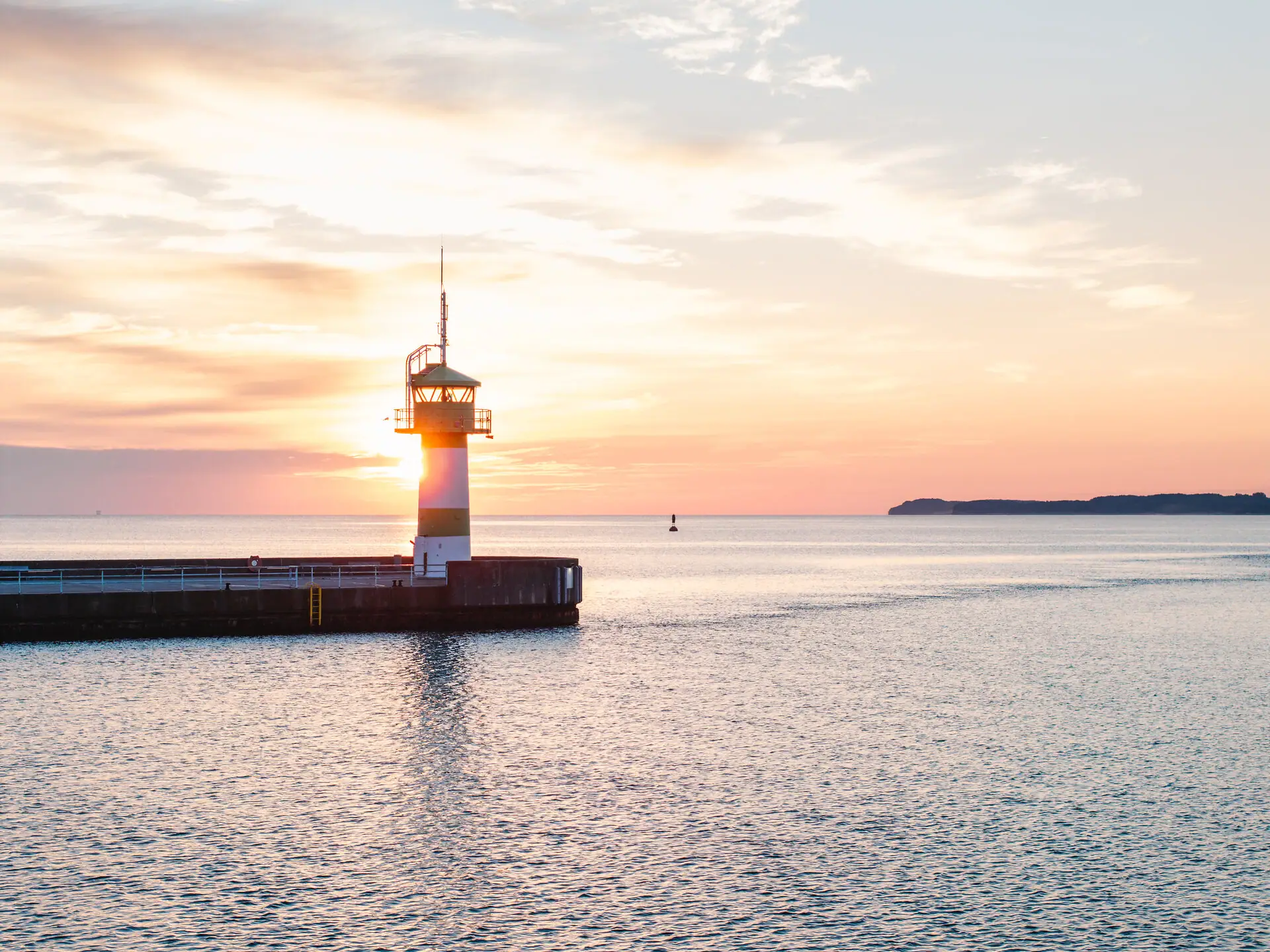 A lighthouse on a jetty in the middle of the ocean.