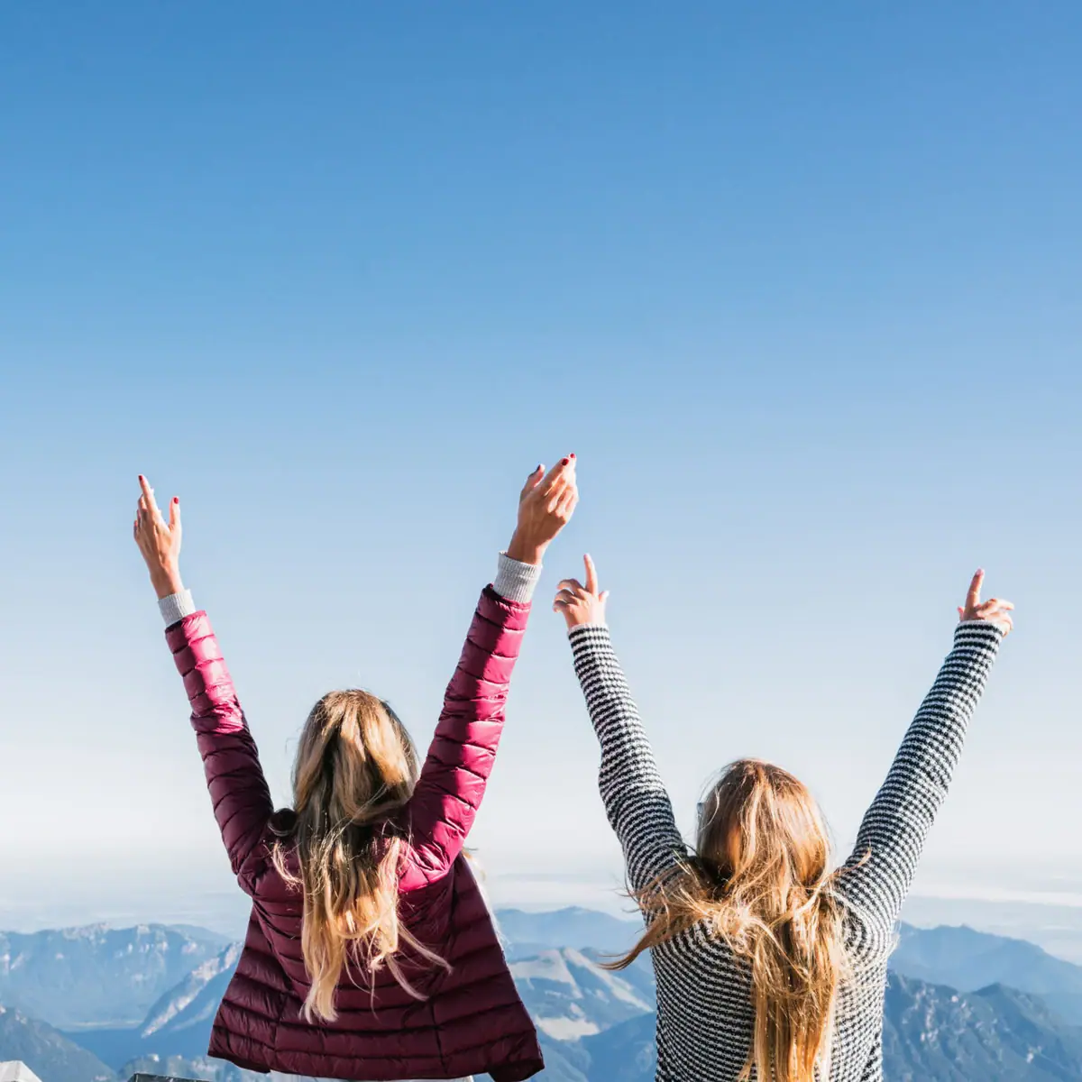 View Zugspitze Two women are standing on a mountain with their arms raised.