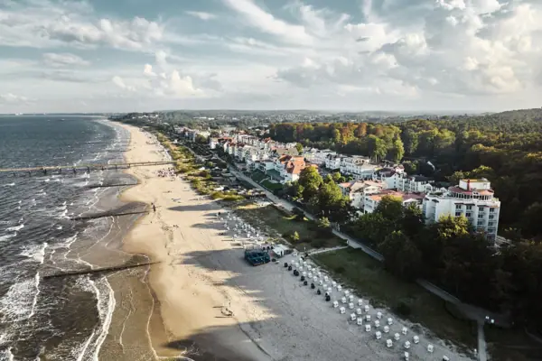 Beach with buildings and trees in the foreground, sky with clouds in the background.