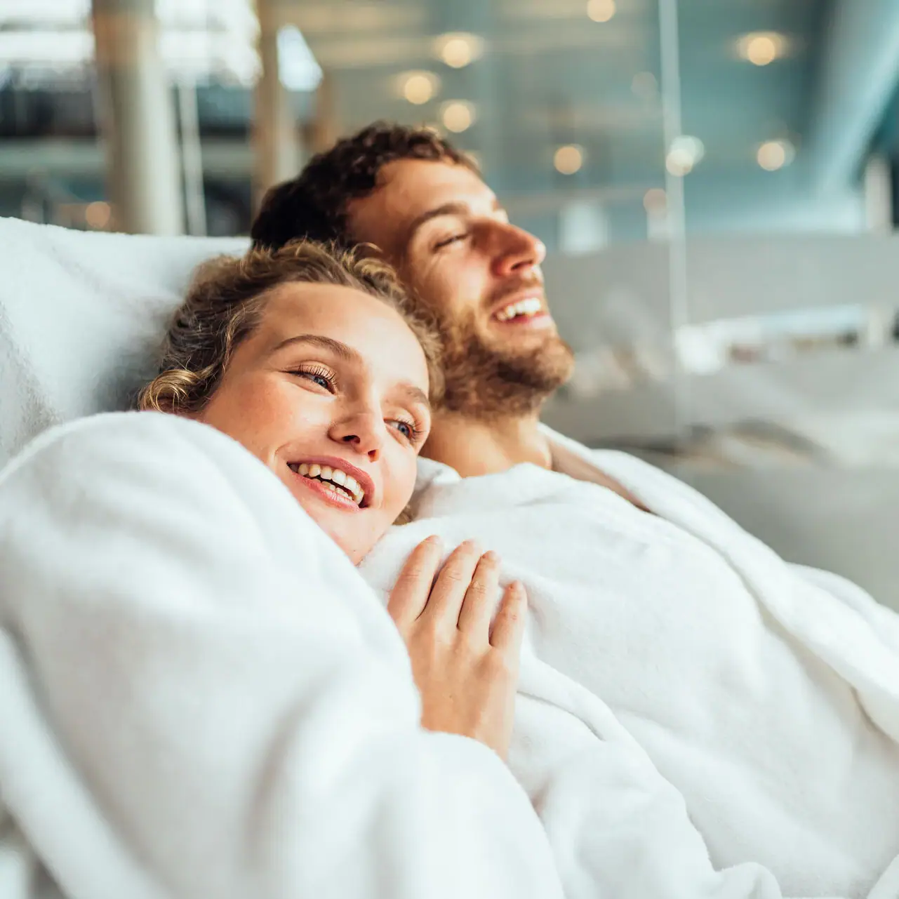 Couple in bathrobe A man and a woman lie smiling in a bed.