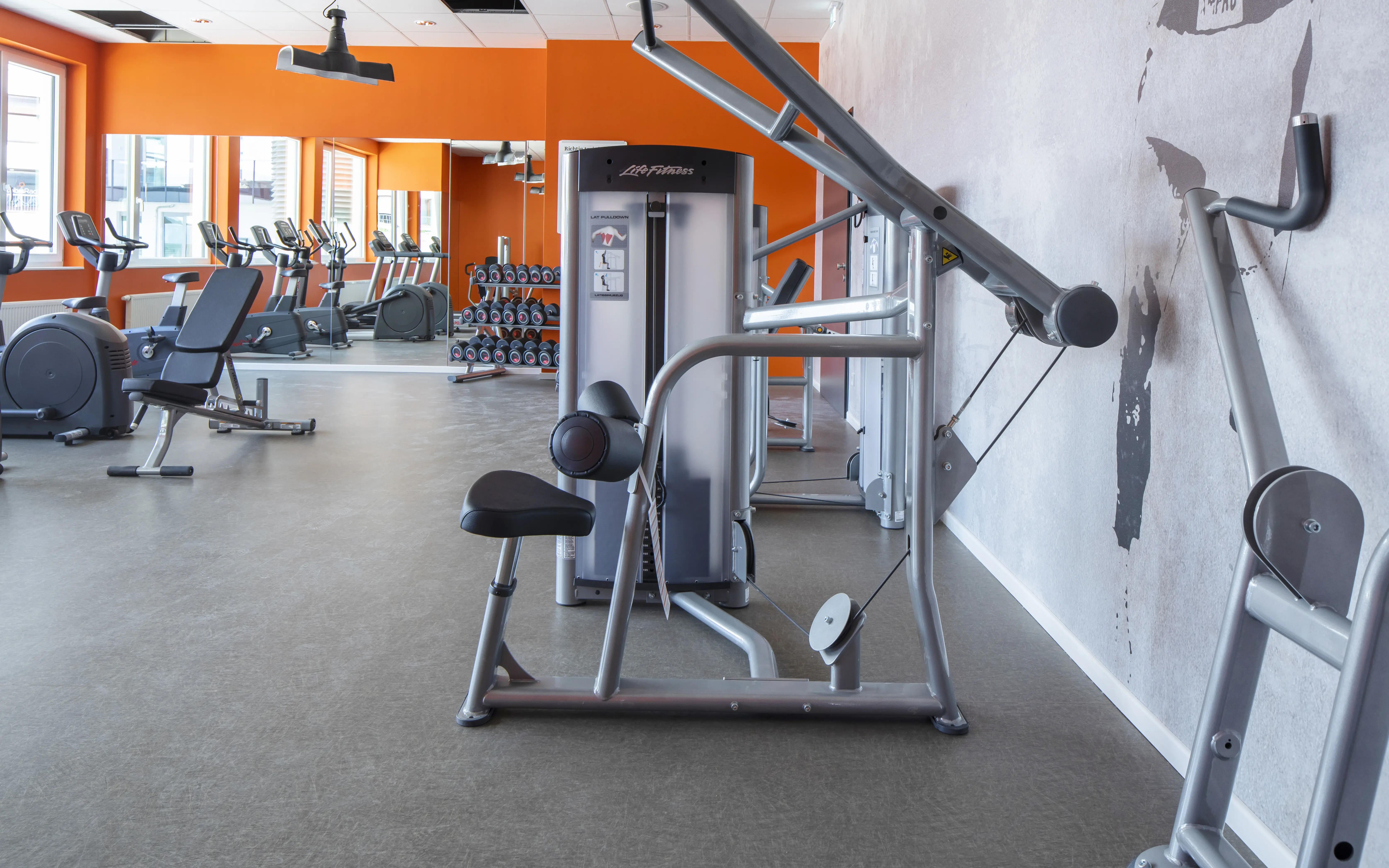 A modern gym featuring state-of-the-art workout equipment, vibrant orange accents, and a mirrored wall reflecting the bright and inviting fitness space.