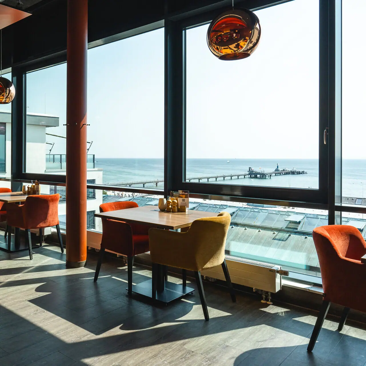 The aja restaurant in Grömitz with tables and chairs and a window with a view of the Baltic Sea and the pier.