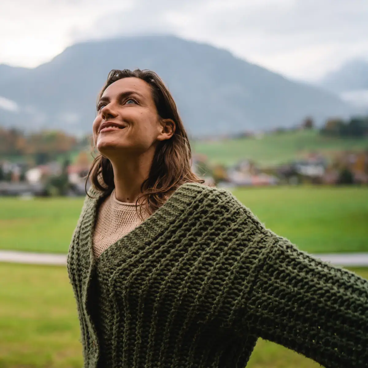 A woman stands in a field with her arms outstretched.
