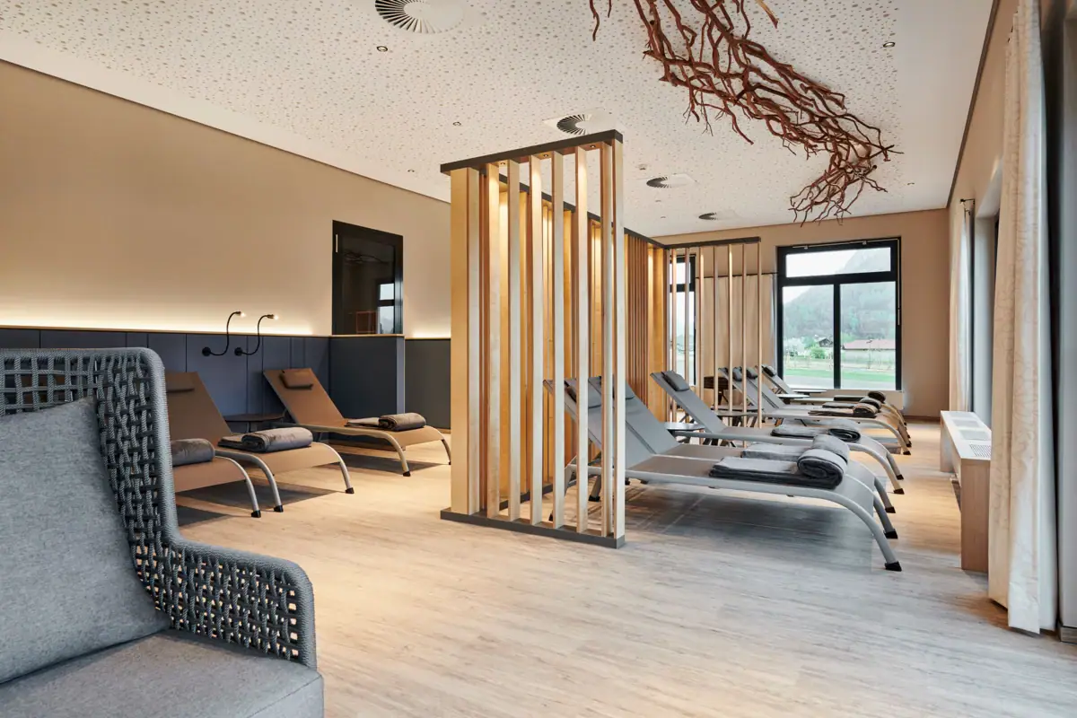 Relaxation area in the sauna landscape at the aja SPA Ruhpolding A room with lounge chairs and a wooden structure.