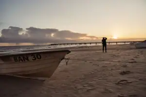 A person stands on the beach next to a boat.