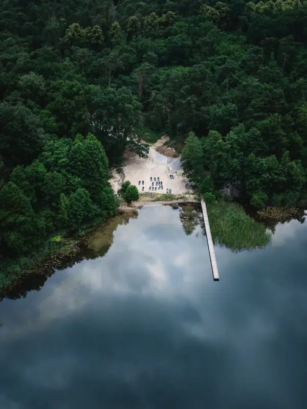 Beach by the lake A body of water with a footbridge and trees in the foreground.