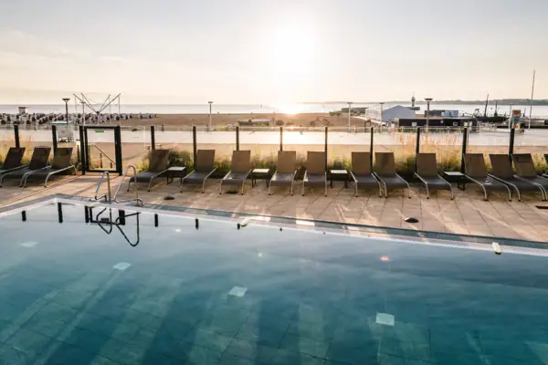 A pool with chairs and a beach in the background.