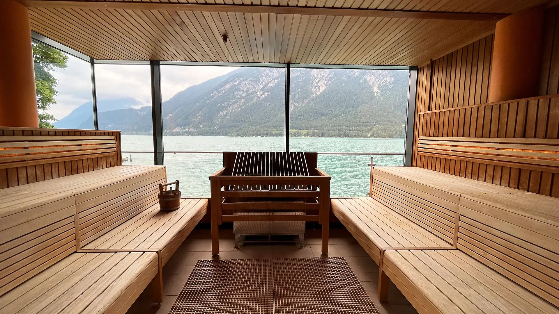 Room with a large window overlooking water and mountains, featuring wooden furniture.