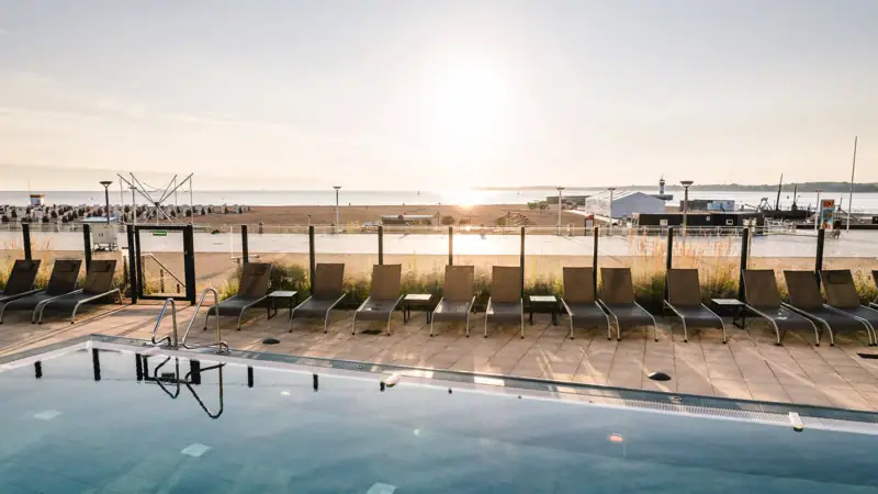 Wellness with a view in Travemünde  A pool with chairs and a beach in the background.
