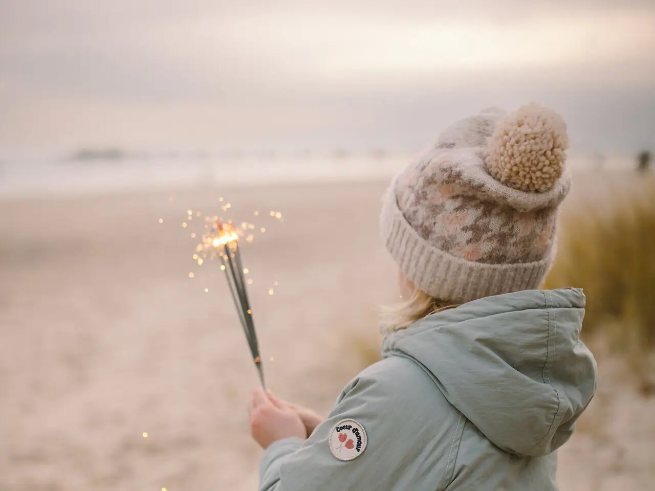 A girl holds sparklers on the beach.