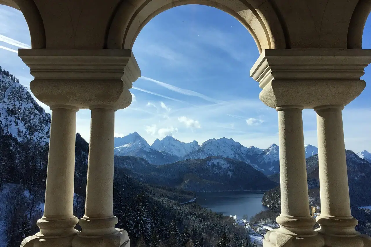 Neuschwanstein Castle View View from Neuschwanstein Castle through a stone arch with a view of mountains and a lake.