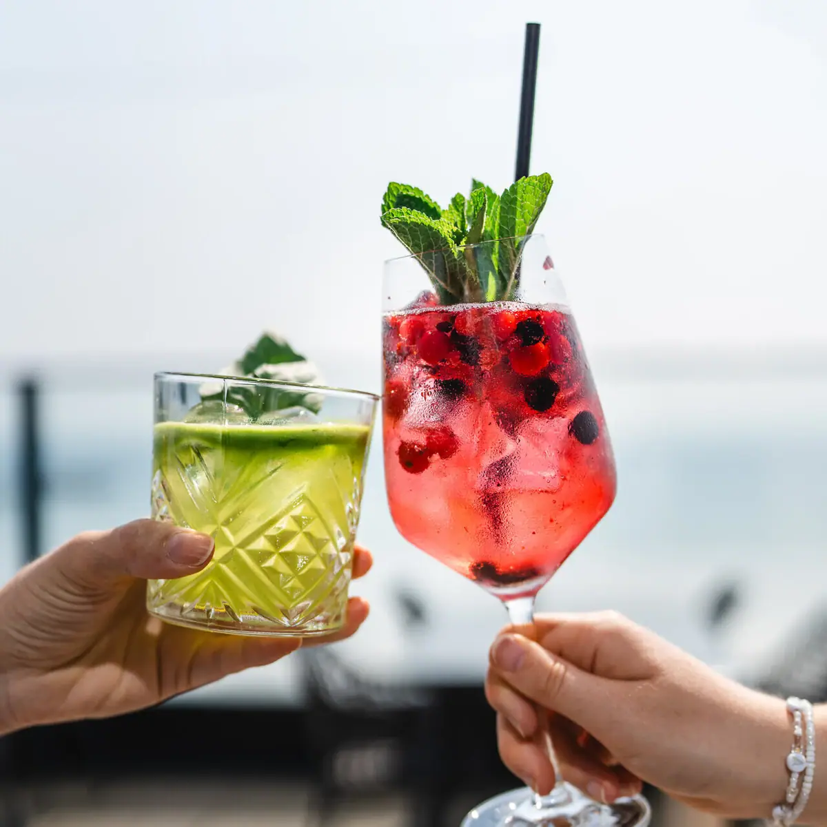A pair of hands holding cocktails with fruit garnish.