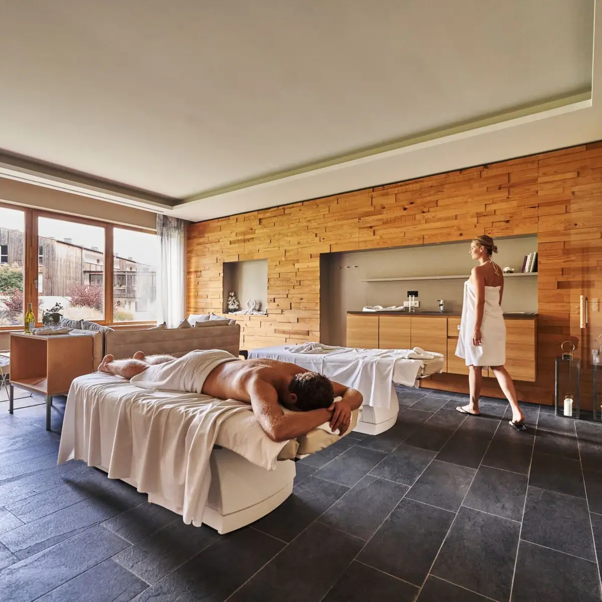 Massage A man lies on a bed while a woman stands behind him.