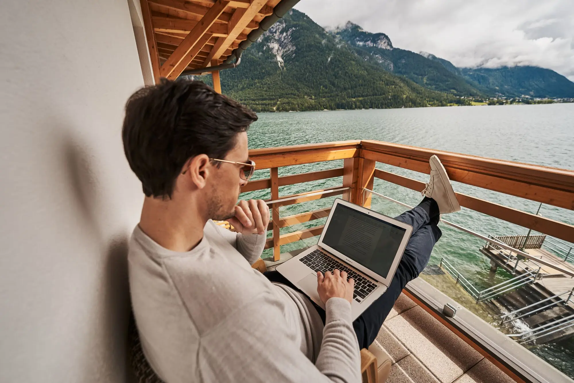 Man sitting on a veranda with a laptop on his lap.