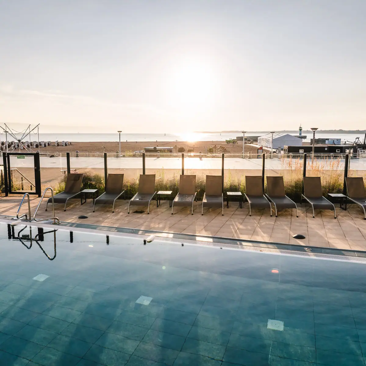 Outdoor pool with beach view A pool with chairs and a beach in the background.