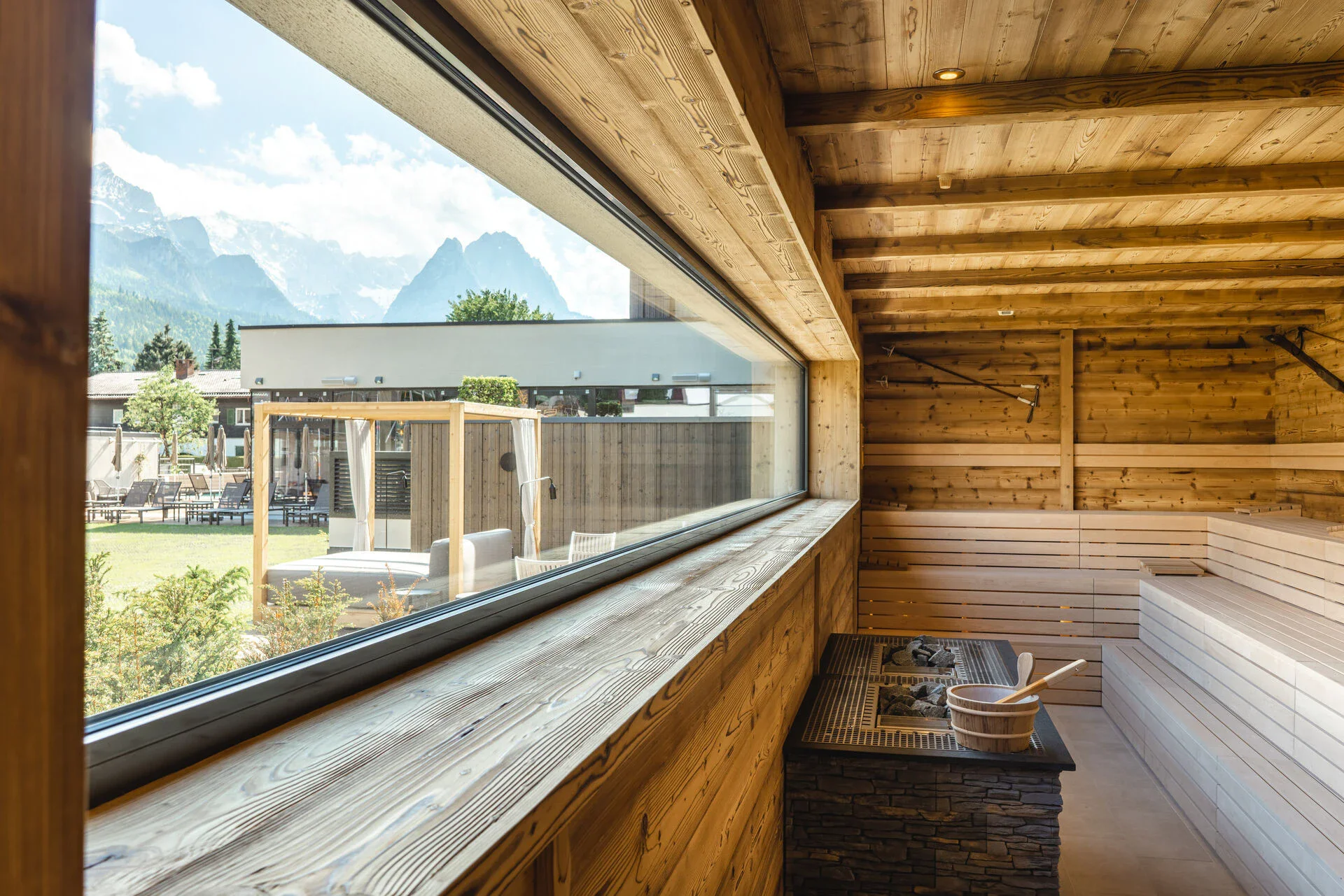 Wooden sauna room with sauna heater in front of a window in a wooden wall with a view of the mountains