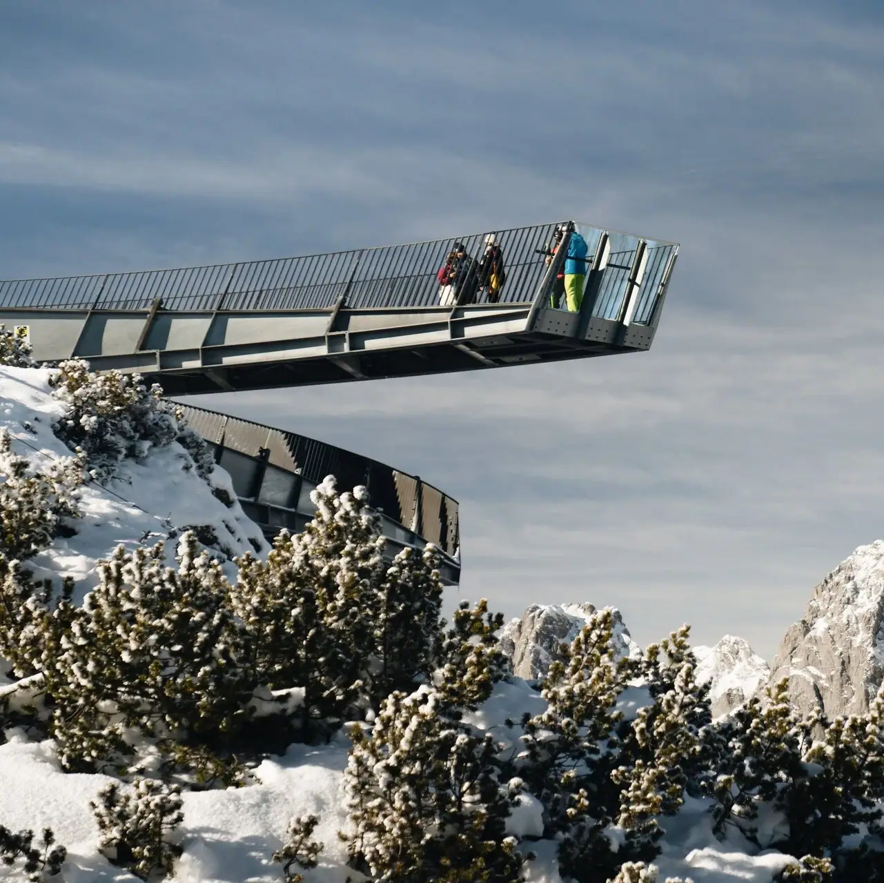 Alpspix People cross a bridge on a snow-covered mountain.