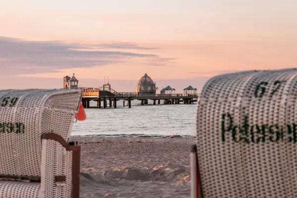 A beach chair on the beach with a pier in the background.
