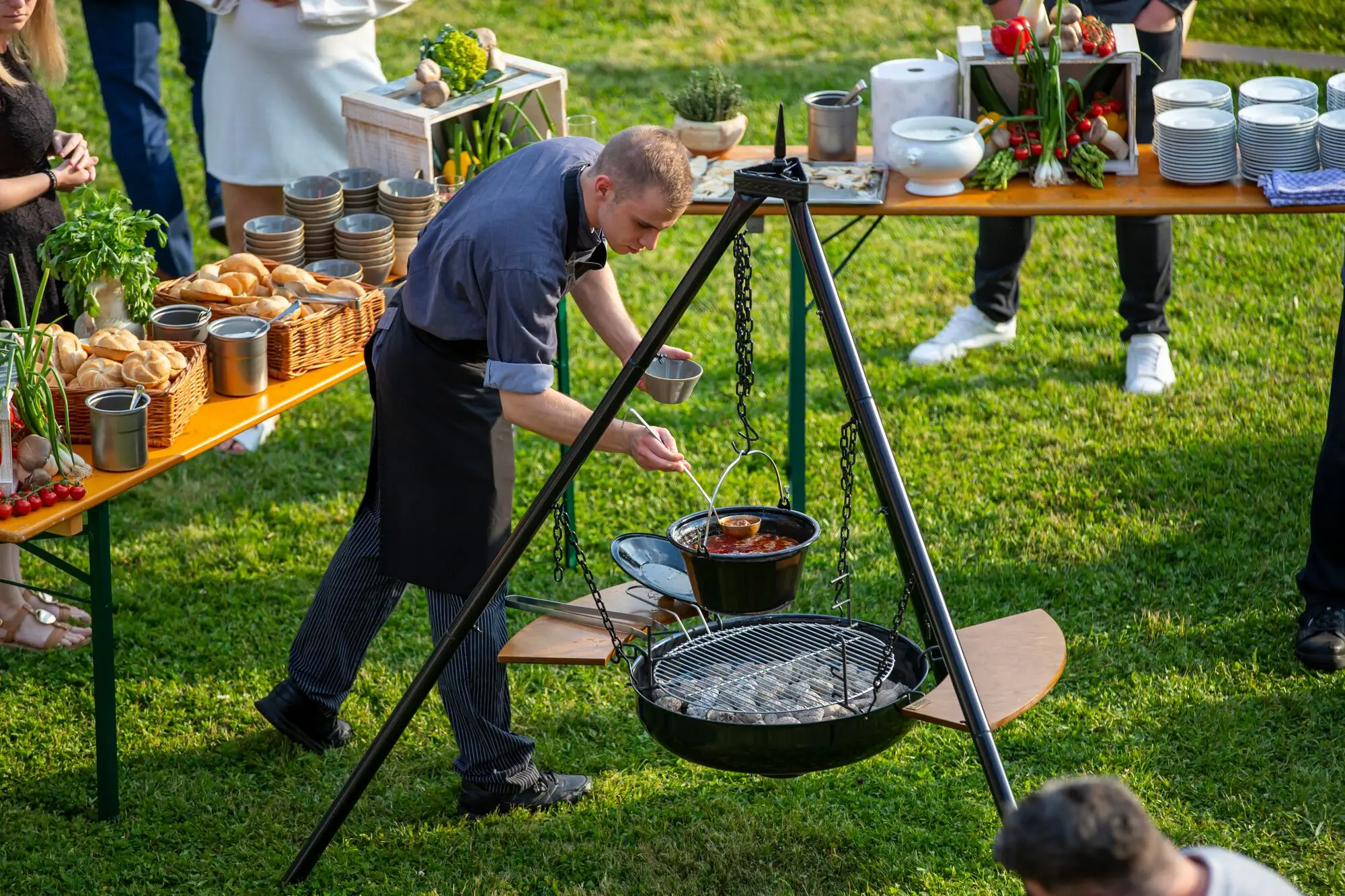 Garden party Cook stands at a large three-legged barbecue and cooks food outdoors.