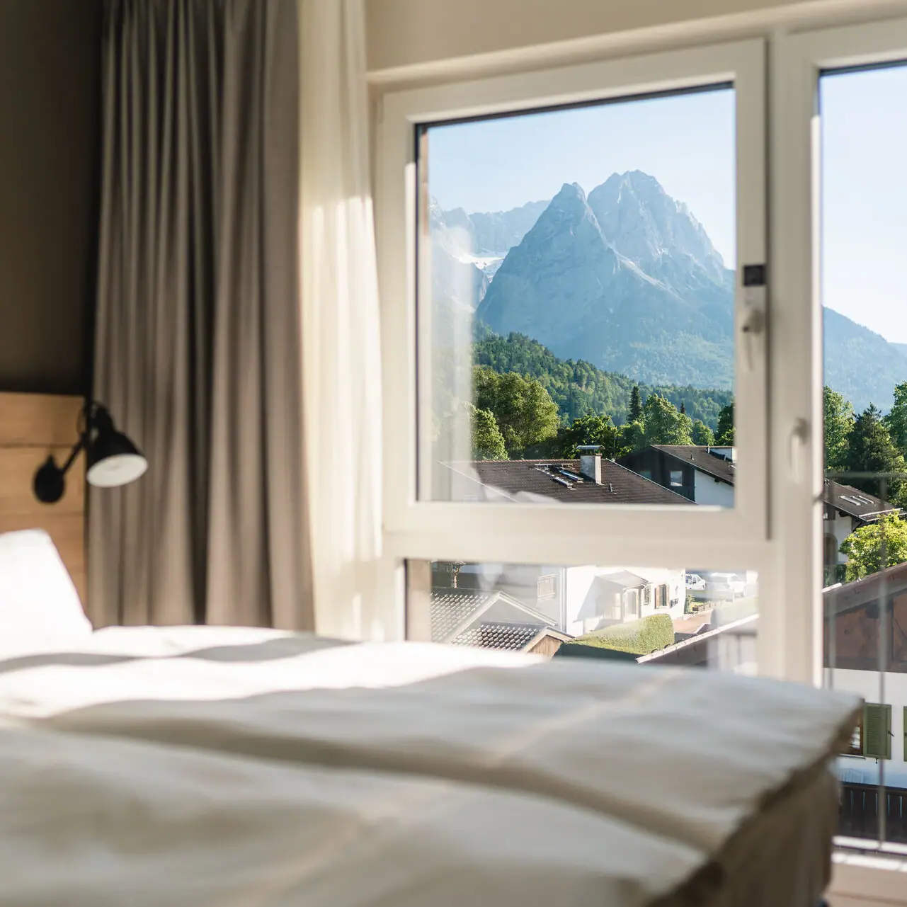 A hotel room at the aja Garmisch-Partenkirchen with a window and a view of the mountains.