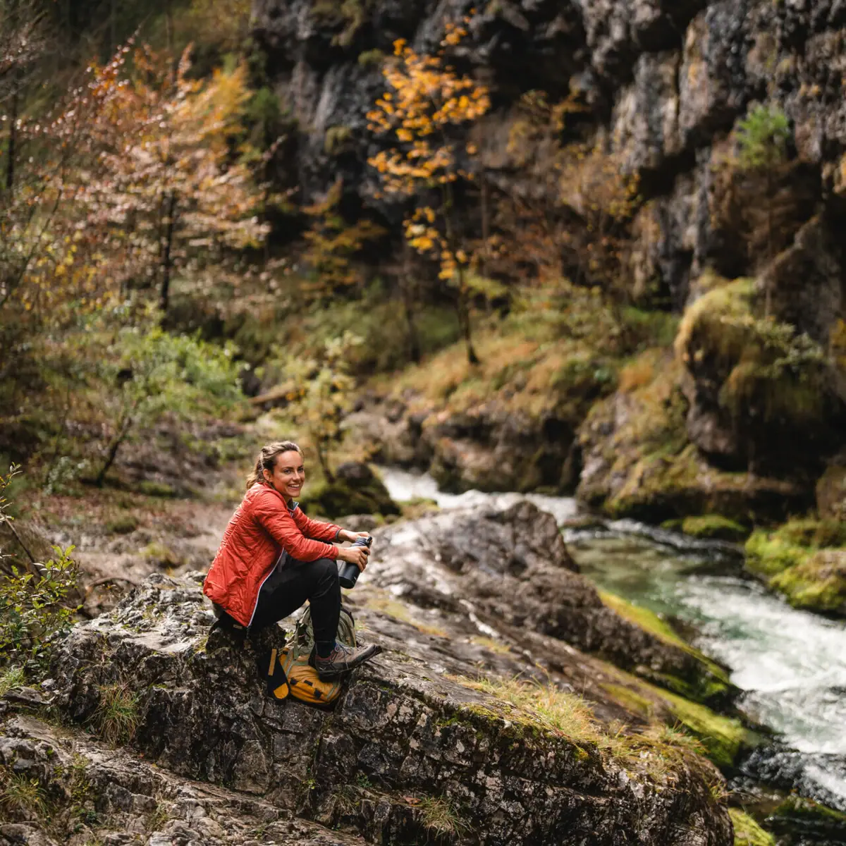 A woman is sitting on a rock by the river.