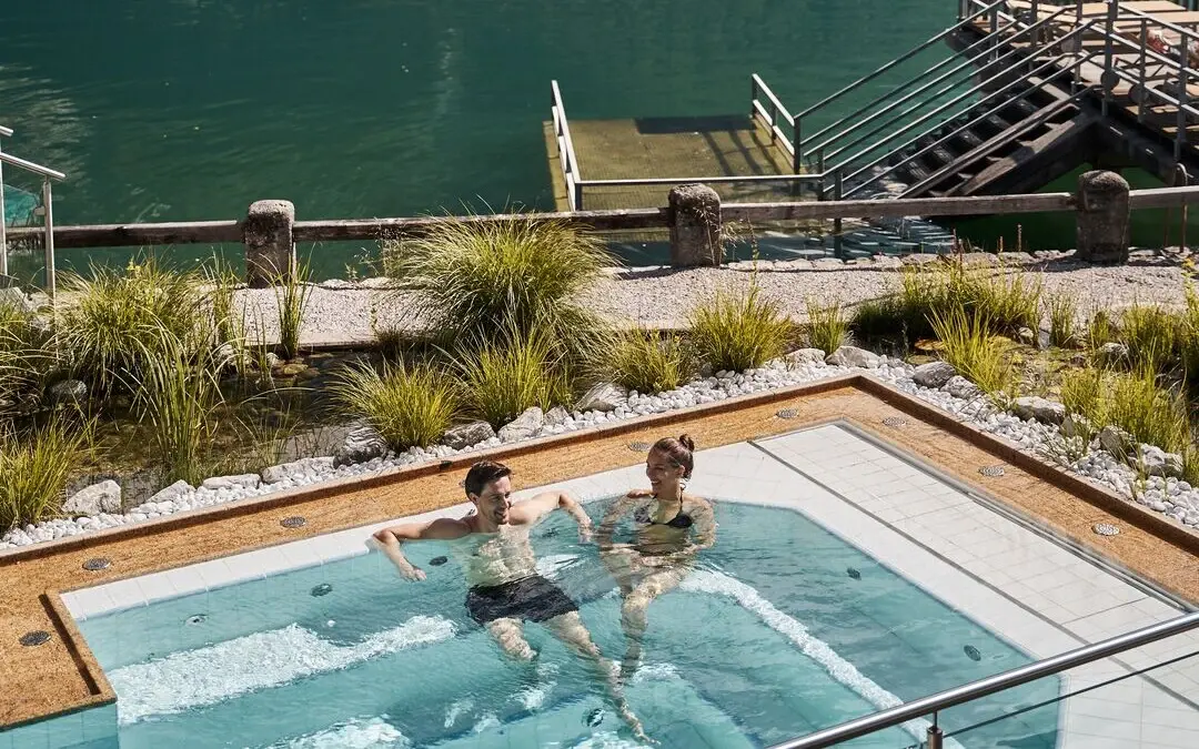 People in the outdoor whirlpool with a lake and mountains in the background.