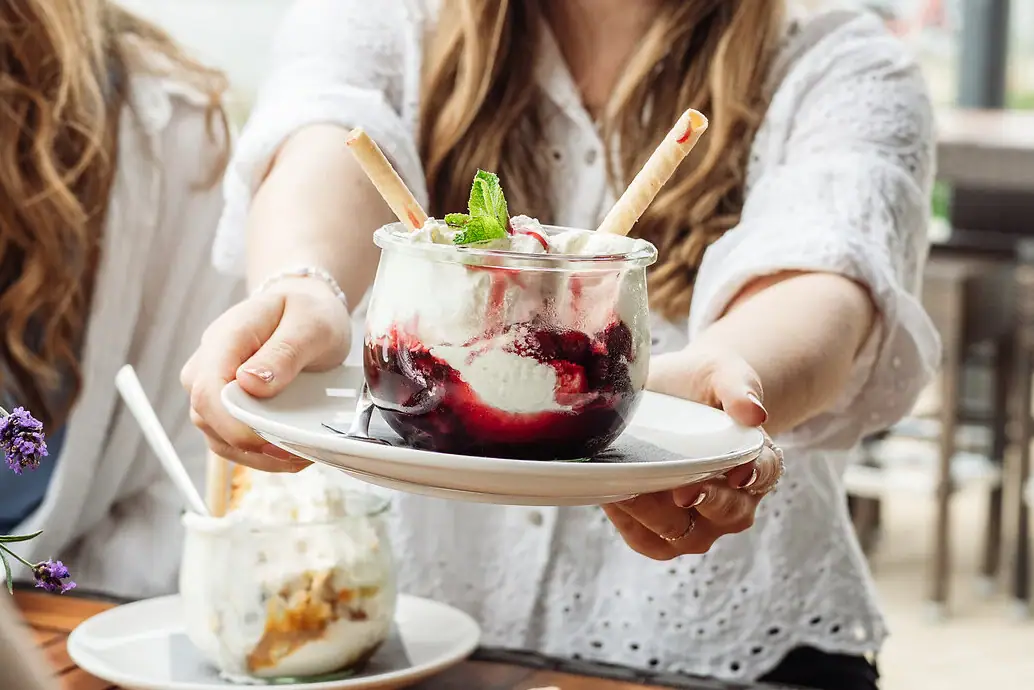 Ice cream at aja Warnemünde A woman holds a plate with a sundae with vanilla ice cream and cherries.