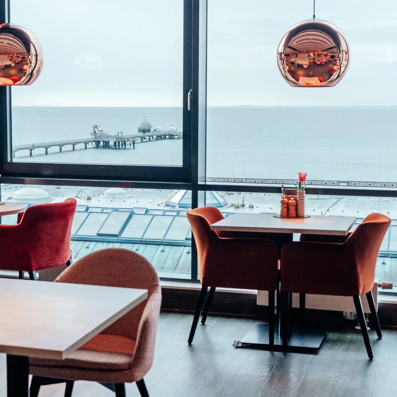 Room with a view of the ocean and a pier through a large window, featuring a coffee table and dining room table.