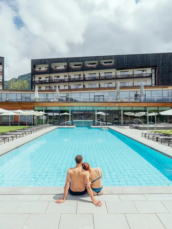A man and a woman are sitting at the edge of a swimming pool.