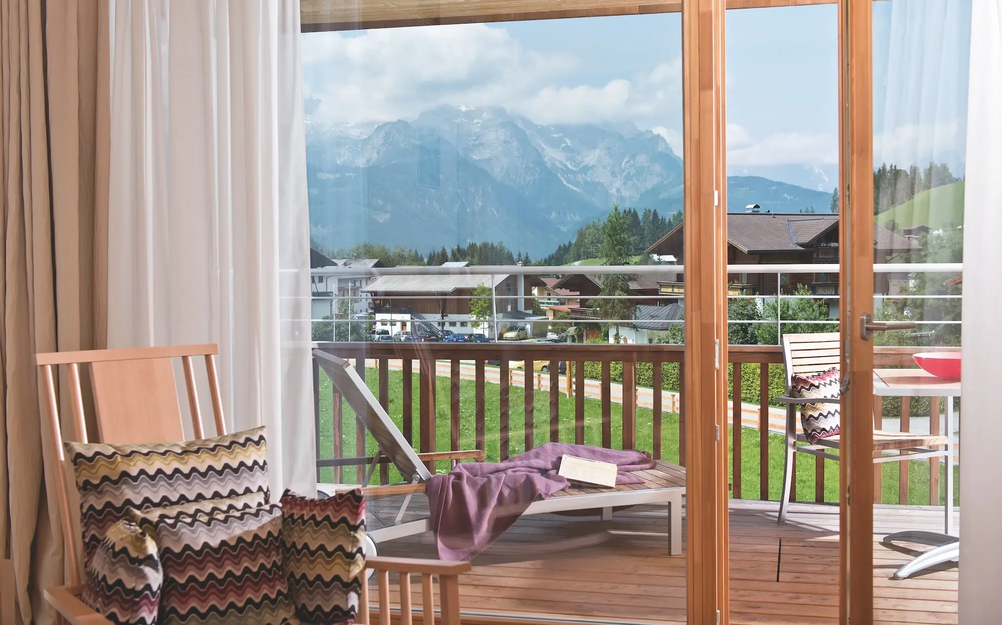 Balcony with view of mountains and trees, furnished with table and chairs.