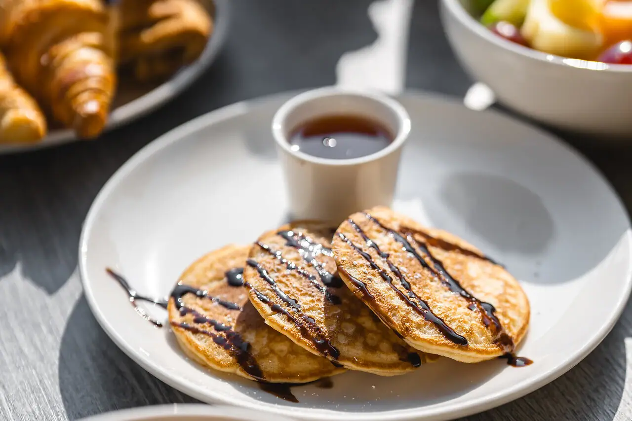 A plate with pancakes and syrup and a cup with syrup.
