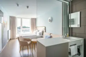 aja Travemünde Zimmer Ein modernes, helles Hotelzimmer mit einem Bett und einem Sofa.