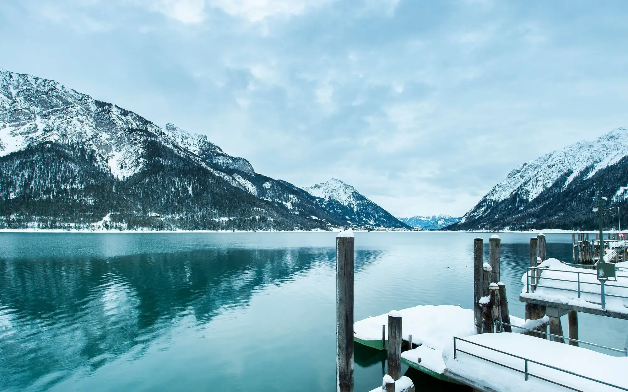 Snow-covered footbridge on Lake Achensee with mountains in the background.