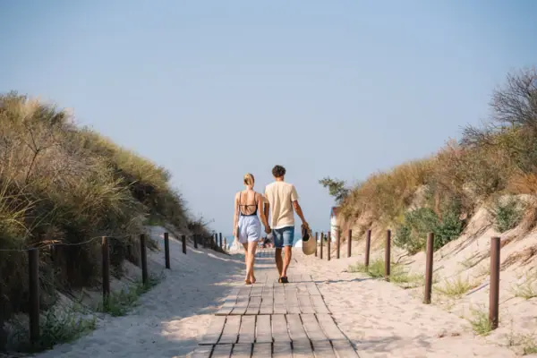 A woman and a man are walking hand in hand towards the beach access point in Warnemünde.