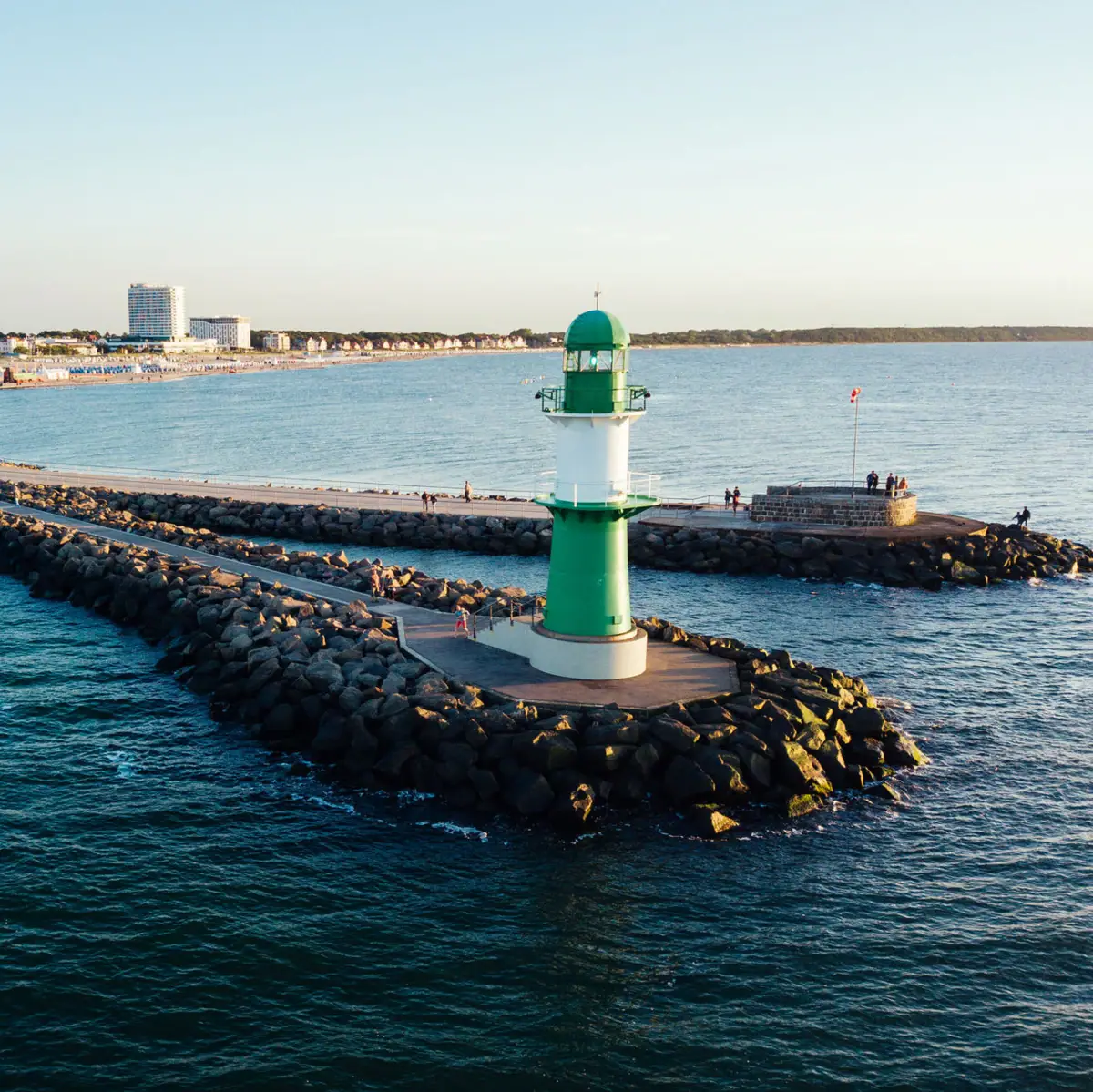 Warnemünde A green and white lighthouse on rocks in the water.