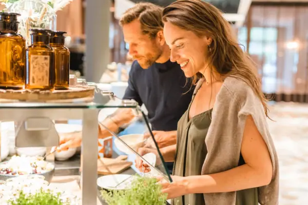 A man and a woman are standing in front of a buffet counter.