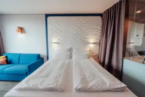 A bed with white sheets and a blue sofa.