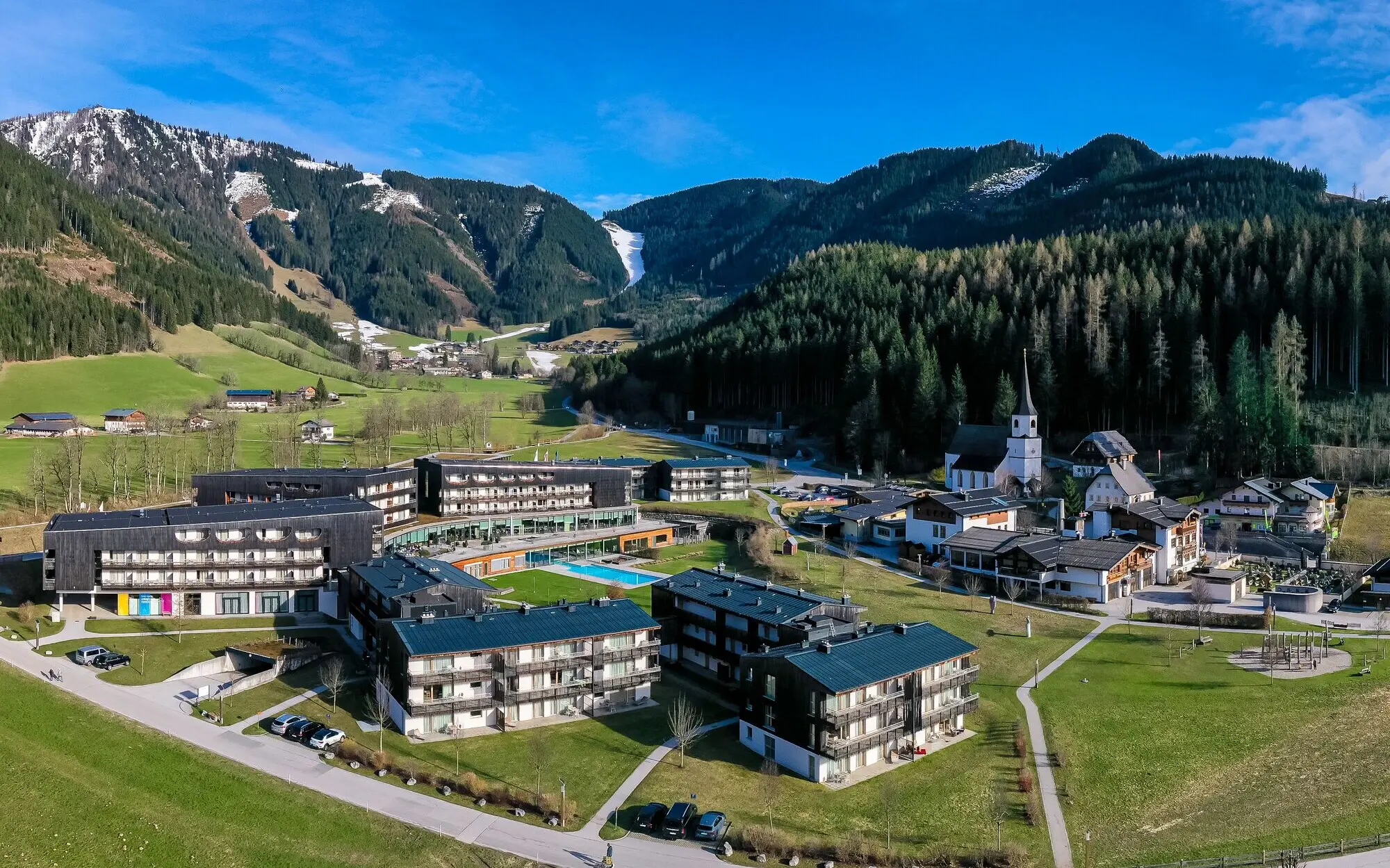 The aja Werfenweng with lawn and swimming pool surrounded by trees and mountains.