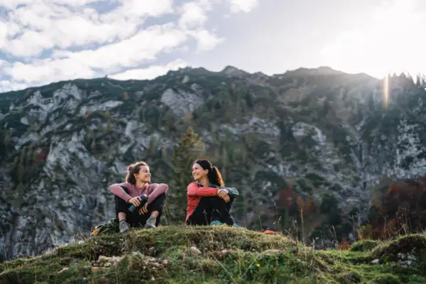 Hiking in Ruhpolding Two women are sitting on a hill with mountains in the background.